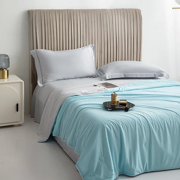 Isblått kyltäcke från NordicBlankets bäddat i stilrent sovrum – visat i helvy med grå satinlakan, beige sänggavel och dekorativ bricka på sängen