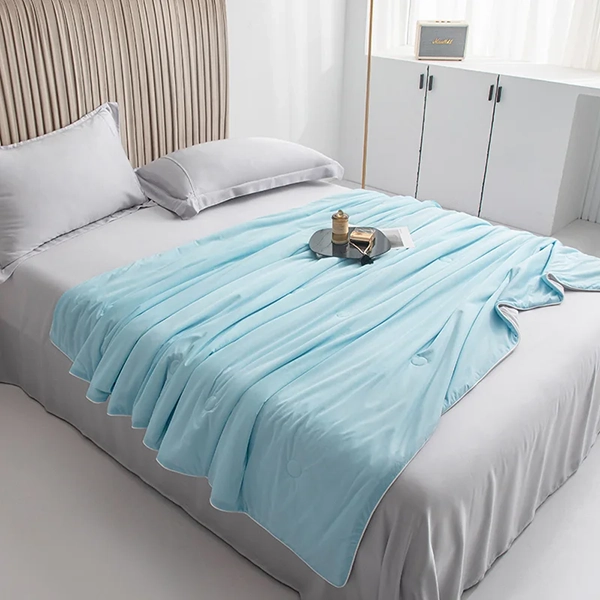 Isblått kyltäcke från NordicBlankets draperat över säng i ljust sovrum – svalkande täcke med silkeslen yta och dekorativ bricka ovanpå