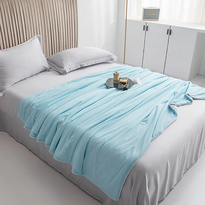 Isblått kyltäcke från NordicBlankets draperat över säng i ljust sovrum – svalkande täcke med silkeslen yta och dekorativ bricka ovanpå