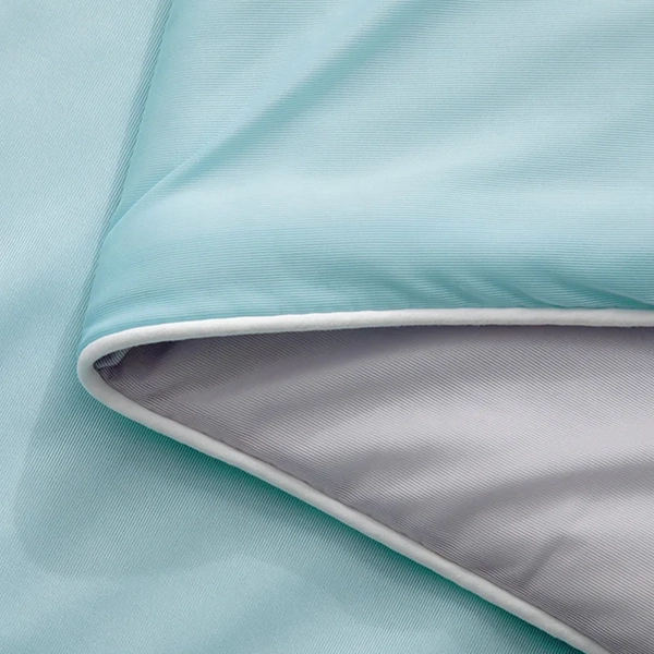 Närbild på dubbelvävd kant av isblått kyltäcke från NordicBlankets – visar kontrasten mellan sval utsida och grå insida i mjukt, andningsbart material